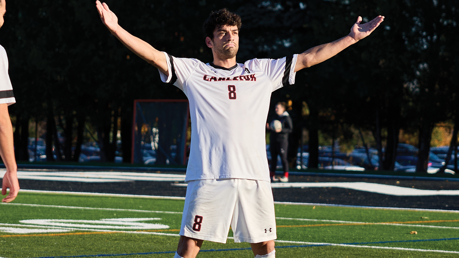 Carleton men's soccer player Luca Piccioli standing in celebration on the field with his arms raised in the air