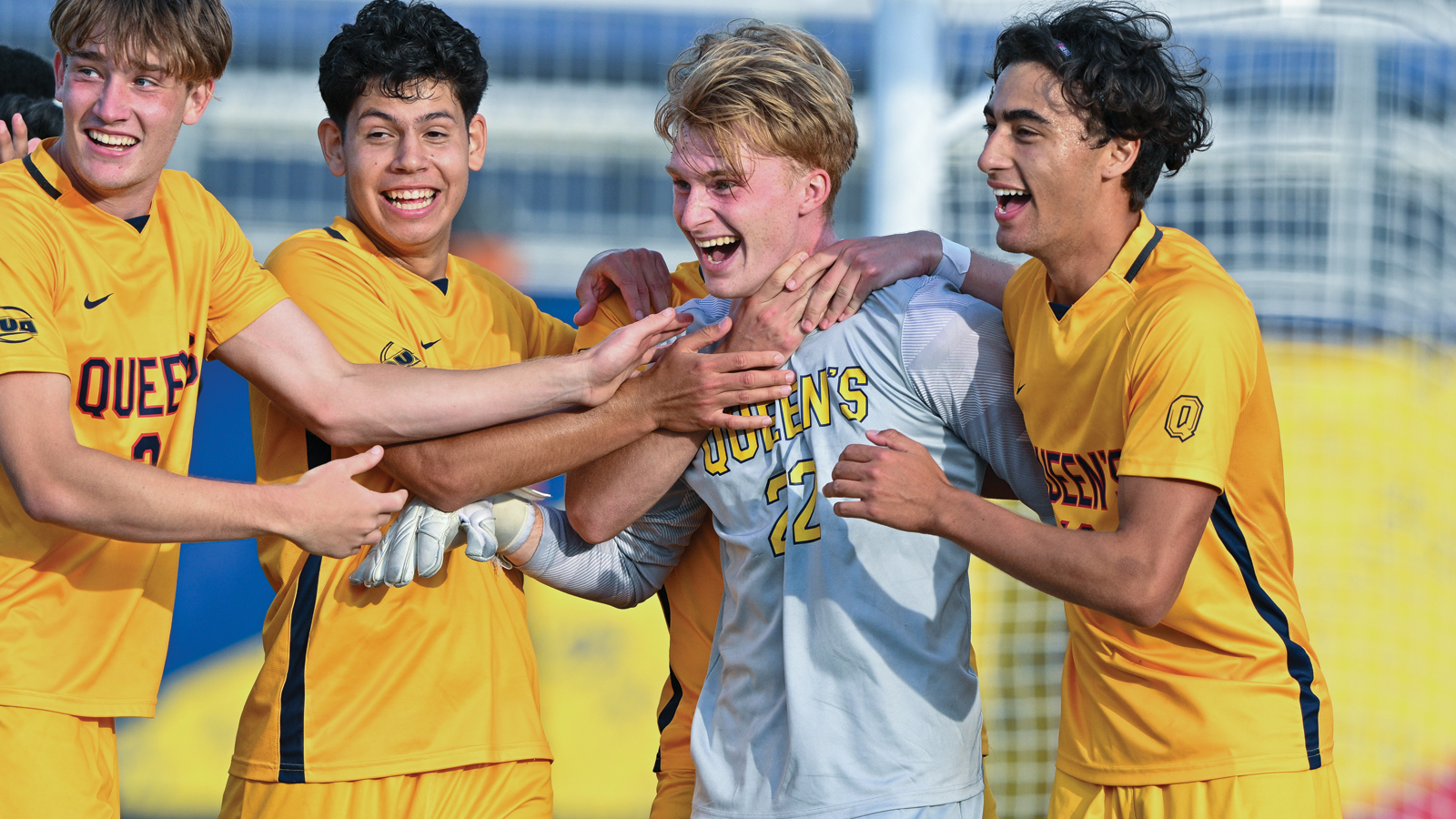 Action photo of Queen's men's soccer players celebrating with and high-fiving goalkeeper Connor Adams