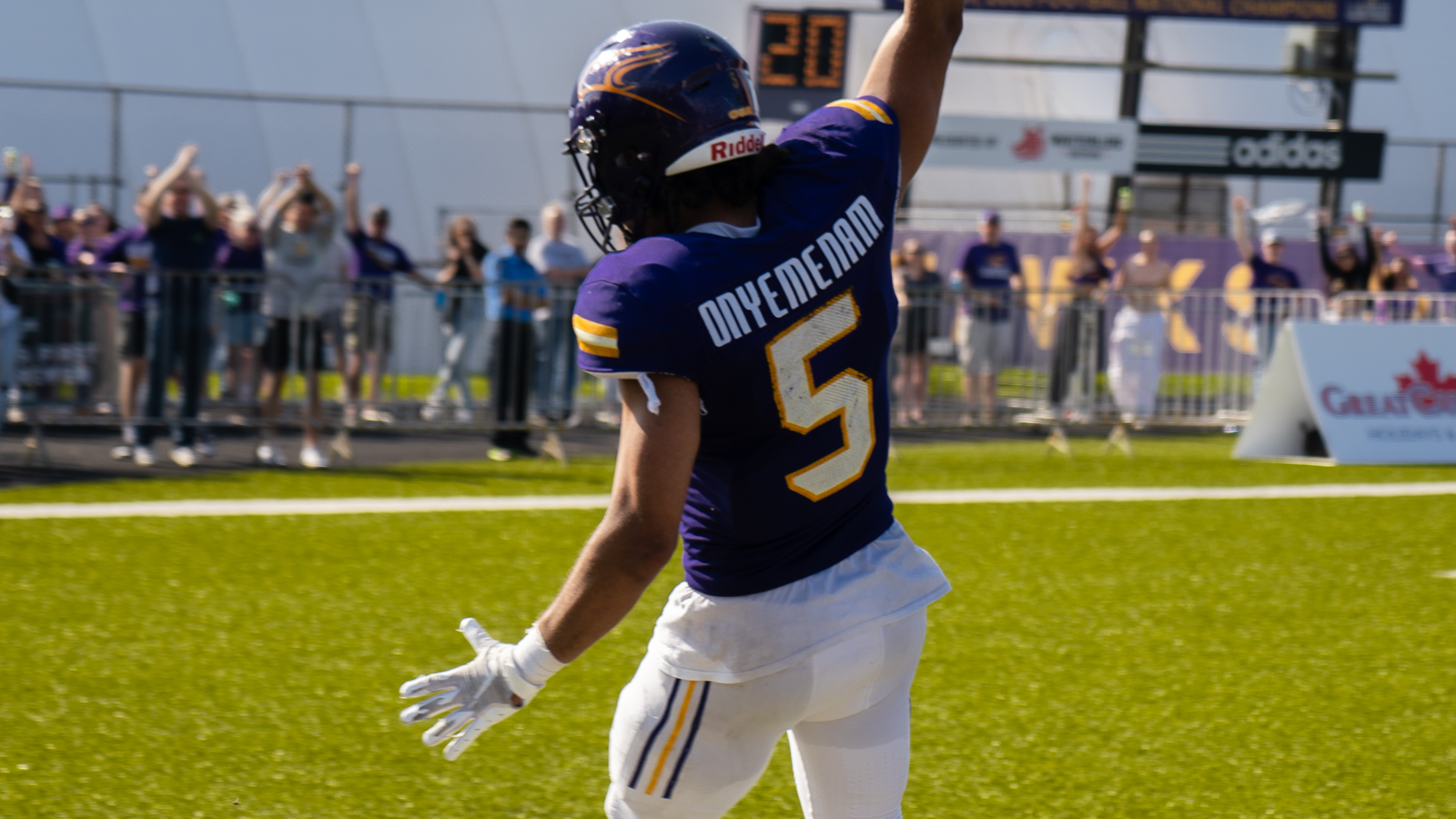 Action photo of Laurier football player Ife Onyemenam holding up the football while running into the end zone