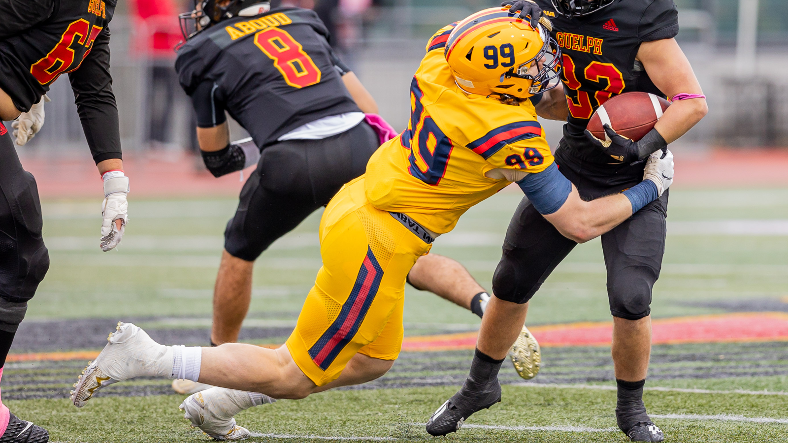 Action photo of Queen's football player tackling a Guelph football player during a game