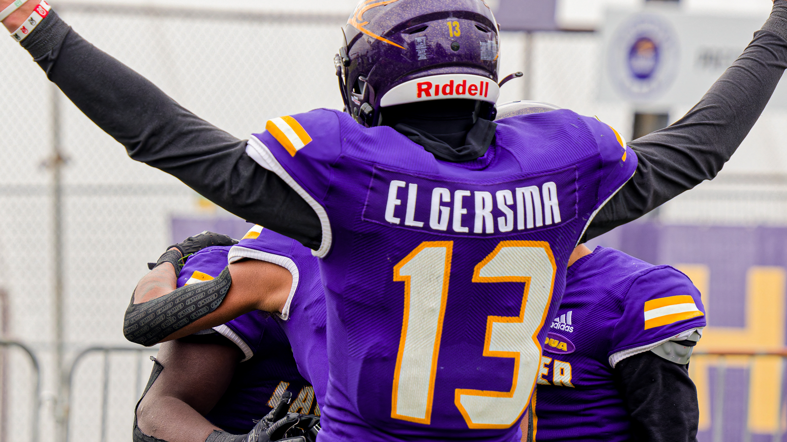 Action photo of Laurier football player Taylor Elgersma facing away from the camera with his arms raised above his head celebrating on the field with his team