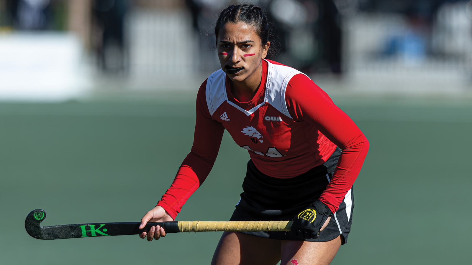 York women's field hockey player in uniform and on the field during a game, looking toward the play while holding her stick horizontally at waist level