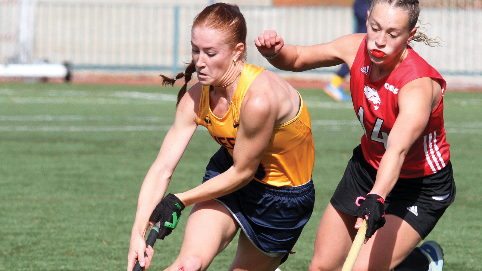 Action photo of Queen's field hockey player running with the ball on her stick as an opposing player tries to defend her