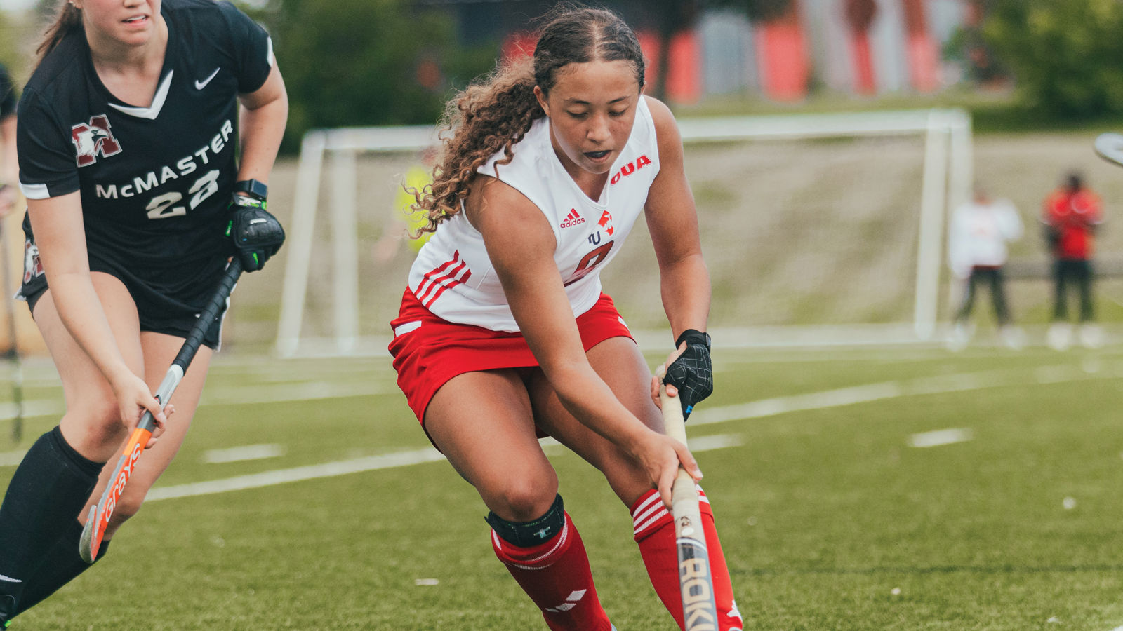 Action photo of York field hockey player running with the ball on her stick during a game as an opposing player tries to defend her
