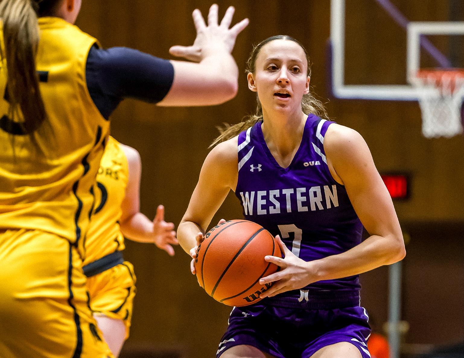 Image of a woman wearing a purple uniform that says Western on it holding a basketball. 