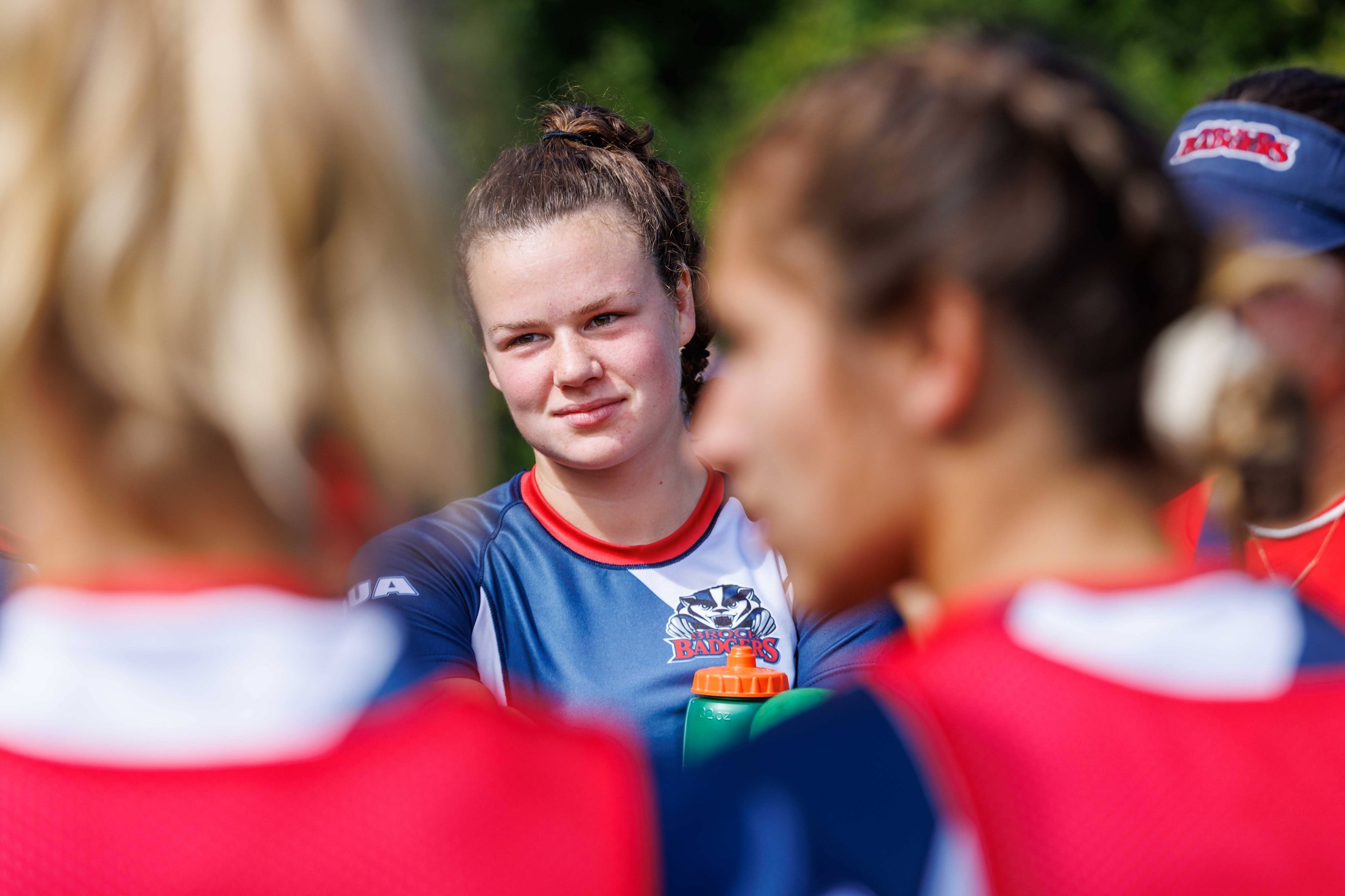  Close-up photo of young woman's face framed by out-of-focus teammates. 