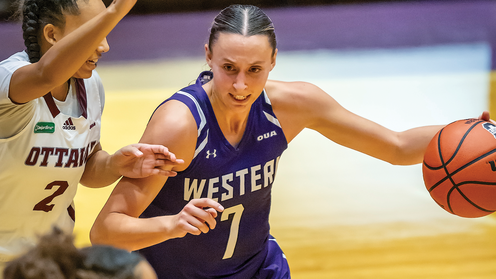 Western women's basketball player MacKeely Shantz dribbling the ball with an opposing defender in front of her