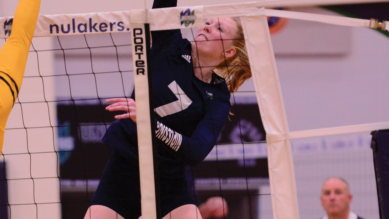 Nipissing women's volleyball player Paige Owen hitting the ball with the net in front of her and the arm of an opposing player going for a block