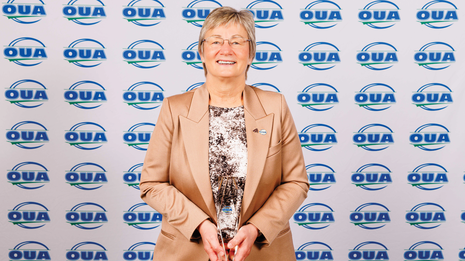 Ottawa's Sue Hylland posing with her OUA Woman of Distinction Award in front of an OUA step-and-repeat backdrop