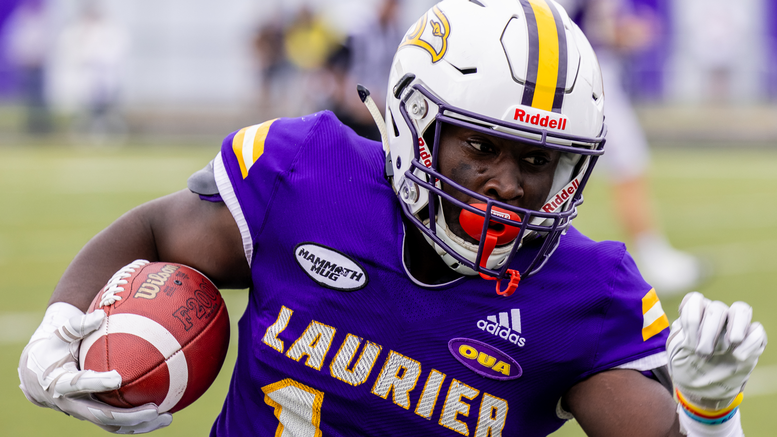 Zoomed in action shot of Laurier running back Quentin Scott running with the ball tucked into his right arm during a game