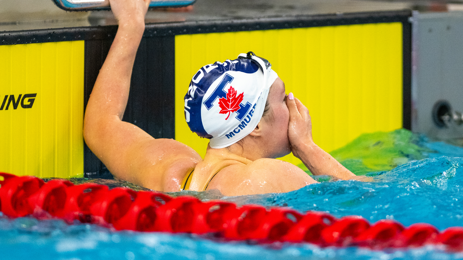 Toronto women's swimmer Ainsley McMurray covering her mouth in excitement while holding on to the wall in the pool after a race
