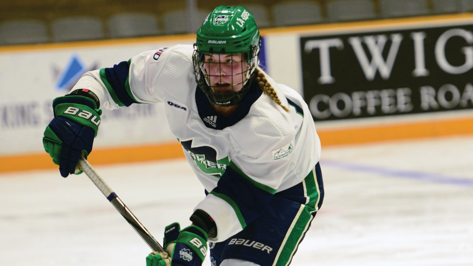 Nipissing women's hockey player Kara Den Hoed skating on the ice during a game while looking downward at the puck on her stick