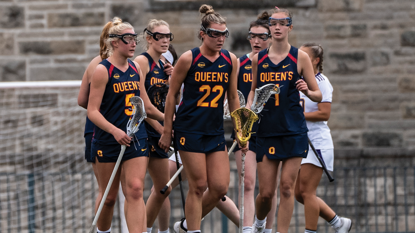 Five members of the Queen's women's lacrosse team walking collectively together after a goal