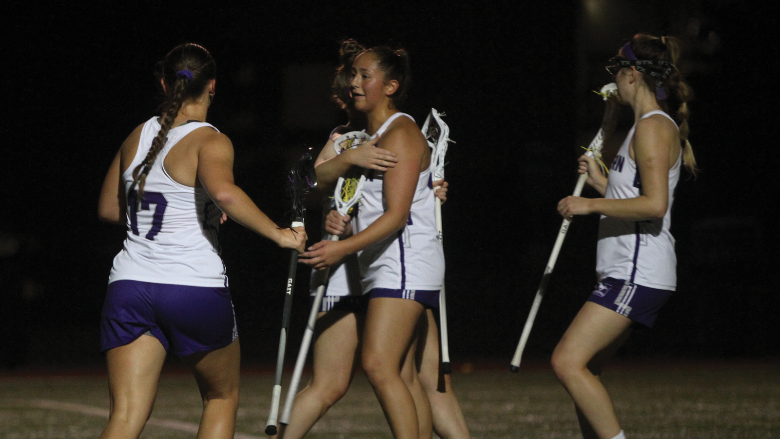 Four members of the Western women's lacrosse team celebrating after a goal with a night sky backdrop