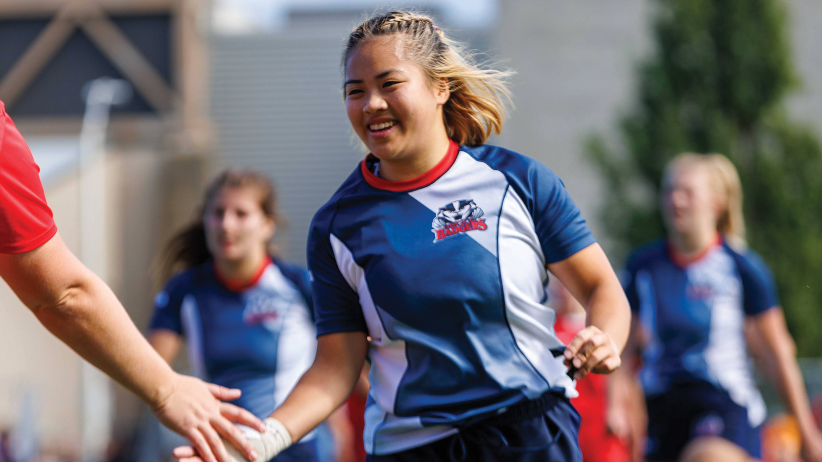 Brock Badgers women's rugby player Farica Truong running on the field in full uniform while giving an outstretched arm a high-five