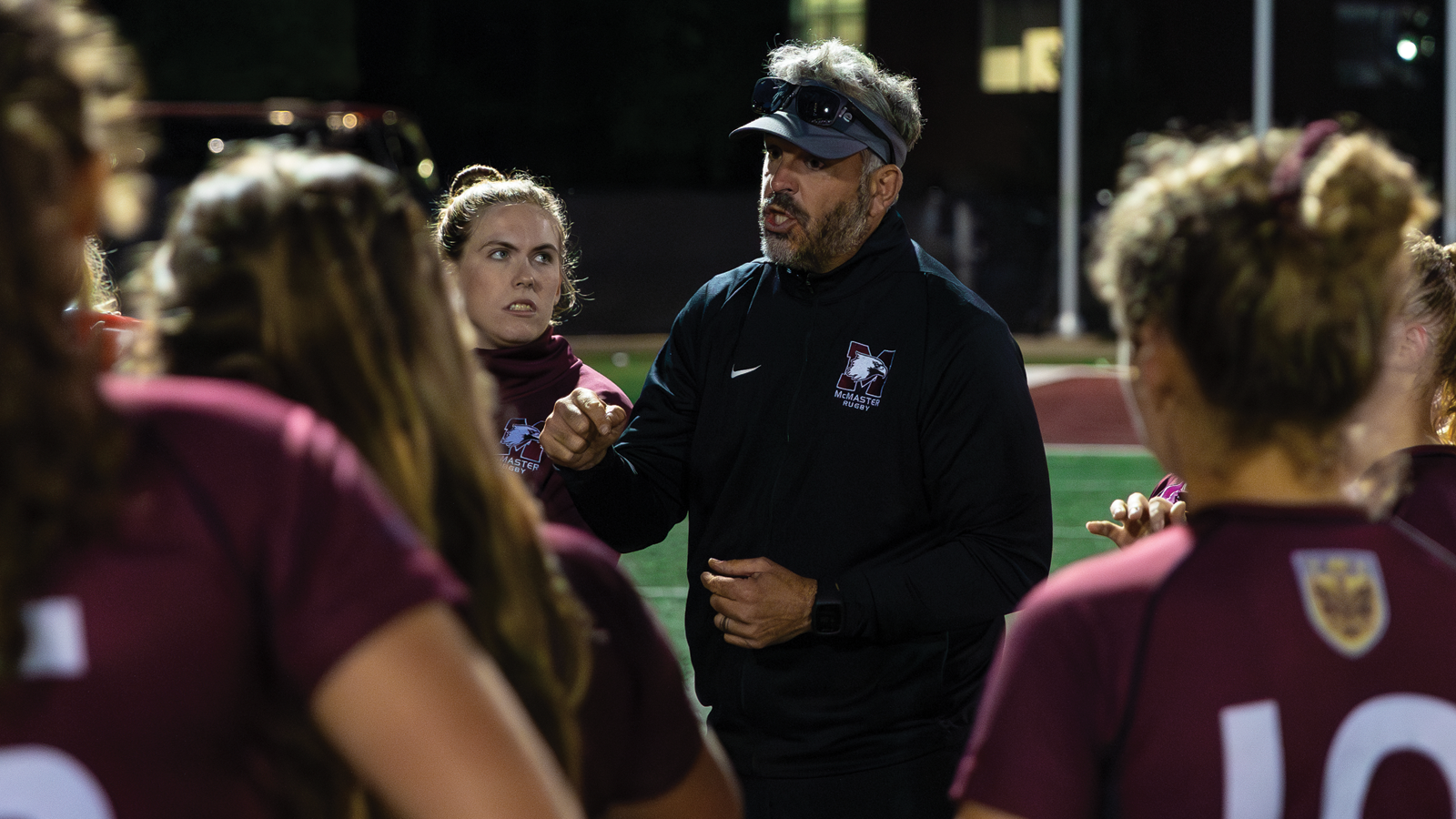McMaster women's rugby coach Chris Jones speaking to his team while they huddle around him