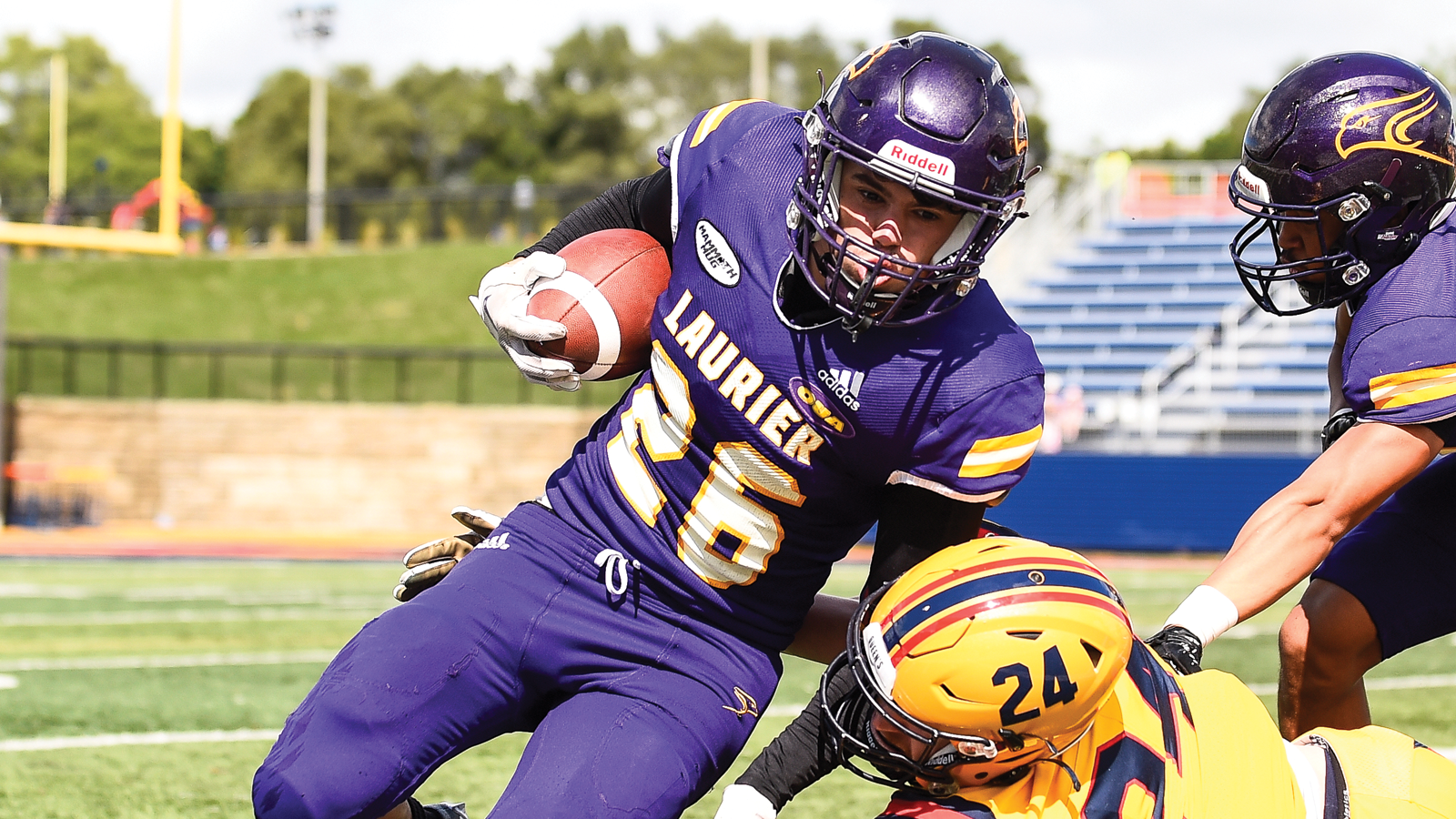 Laurier's Ethan Bayfield running with the ball while being tackled by a Queen's defender