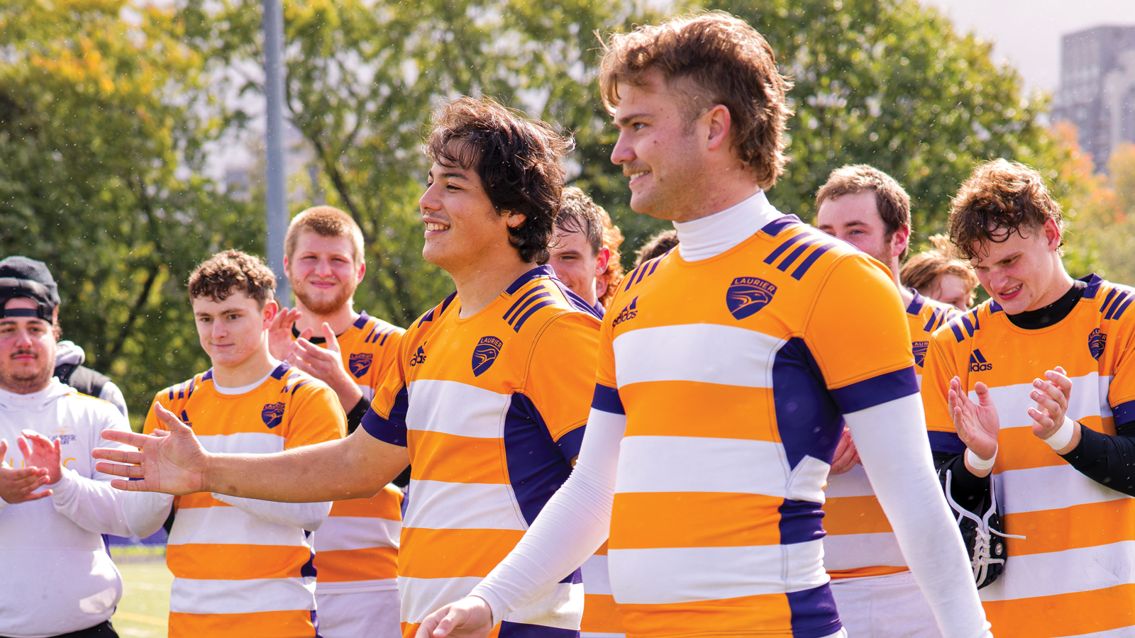 Wilfrid Laurier men's rugby players Dylan Di Girolamo and Adam McNee walking in front of their teammates while they clap