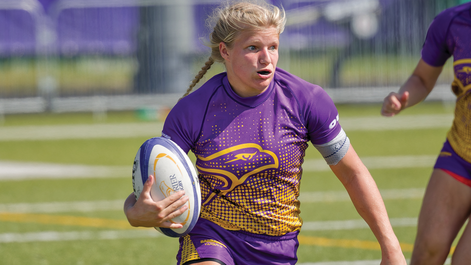 Action photo of Laurier women's rugby player Samantha Hessels running with the ball tucked in her right arm during a game